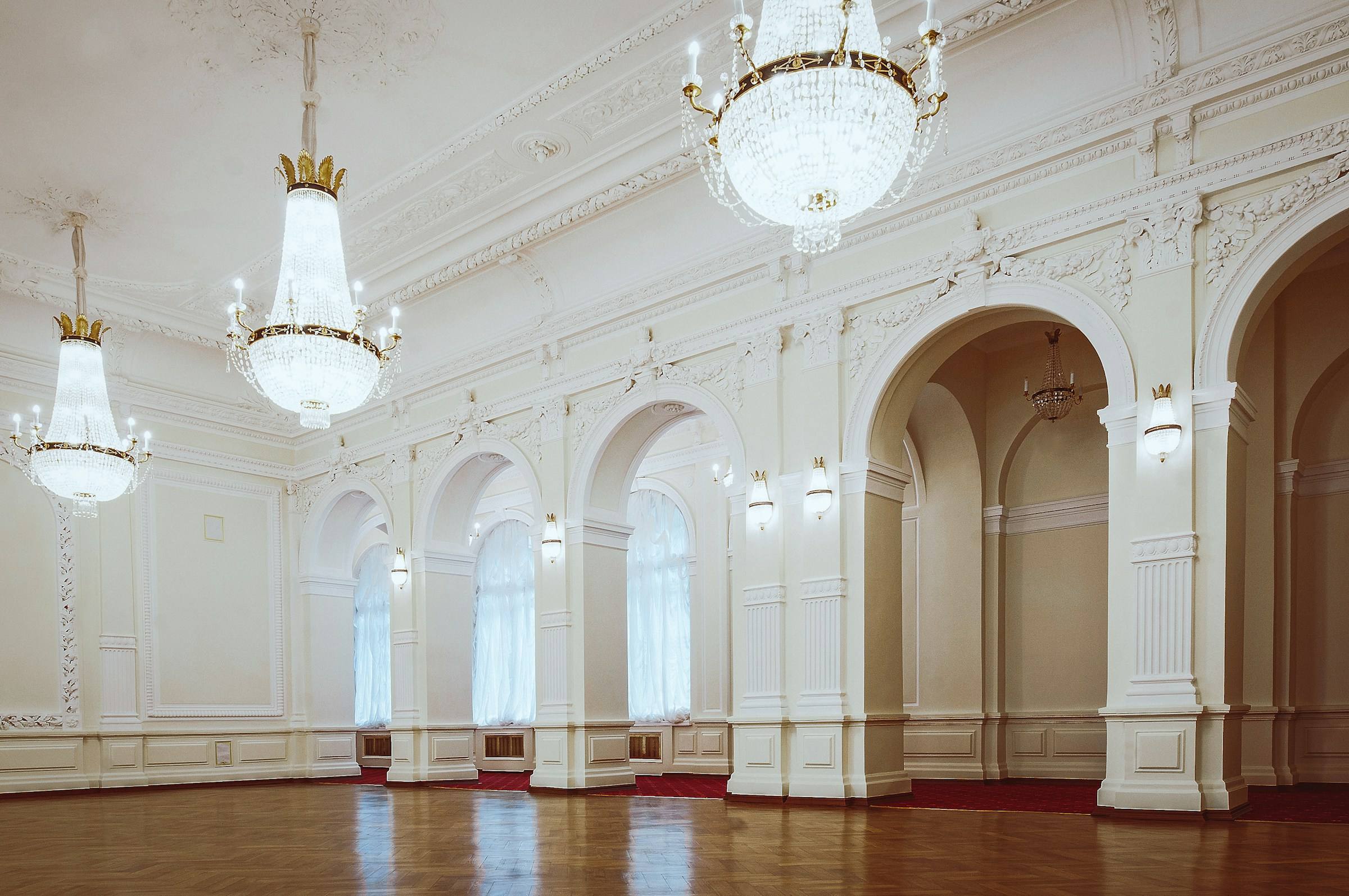 White ballroom with arched doorways, carved pilasters and crystal chandeliers