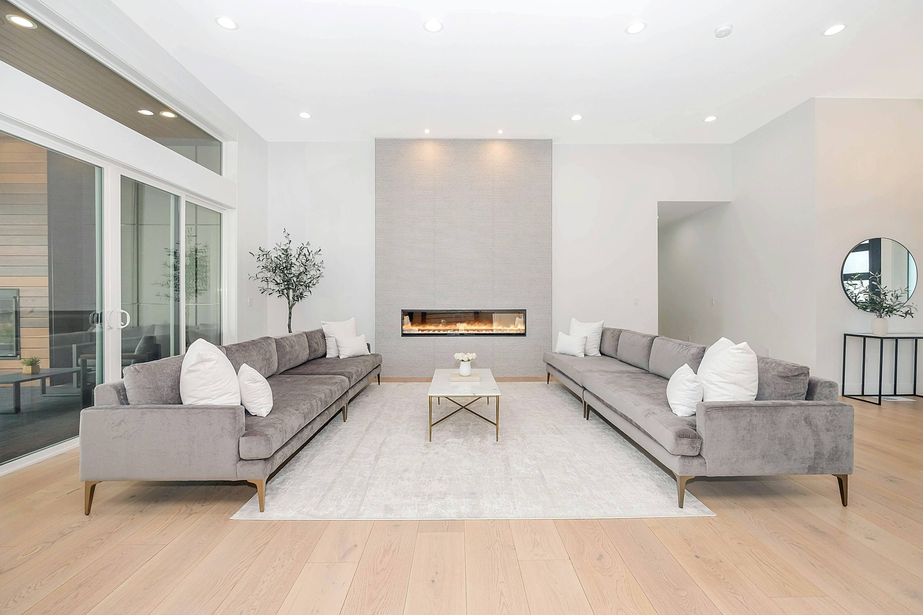 Bright living room with two grey sofas facing each other across a linear fireplace and light oak floors